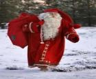 Santa Claus carrying the big bag of Christmas gifts in the woods