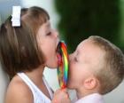 A girl and a boy sucking a big lollipop