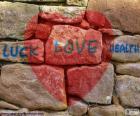 Red heart painted on a stone wall with the text "luck love health"