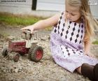 A girl sitting on the ground playing with a red tractor