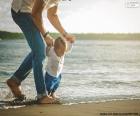 Baby helped by his father, walking along the seashore